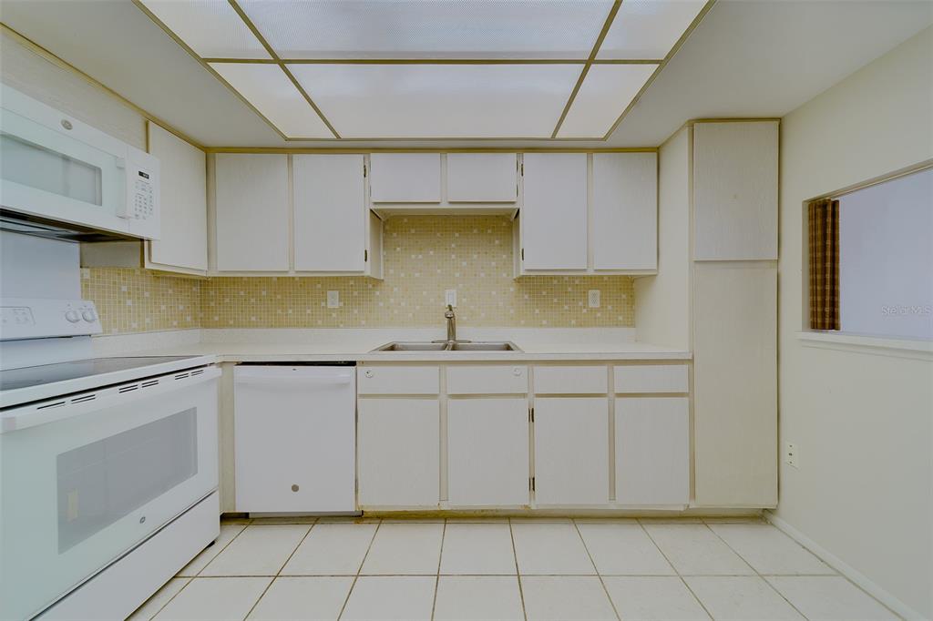 A kitchen features white cabinets, white appliances, a tiled backsplash, and a drop ceiling — 17920 GULF BOULEVARD UNIT 1408, REDINGTON SHORES, FL