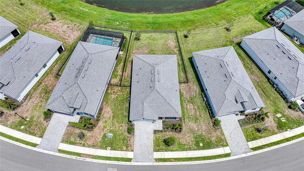 An aerial view shows three suburban houses with gray roofs and paved driveways near a pond — 8268 SHORE LAKE DRIVE, ENGLEWOOD, FL