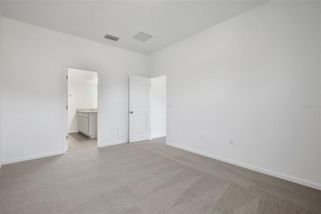 A carpeted bedroom with white walls, two doorways, and a view into an attached bathroom — 2920 SUPERMARINE ROAD, TAVARES, FL