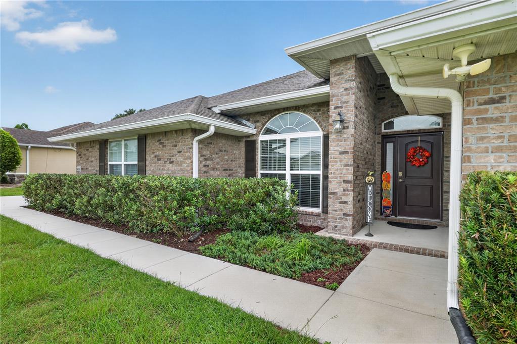 A brick house exterior features a front walkway, a hedge, and a dark entry door — 9636 SW 40TH TERRACE, OCALA, FL