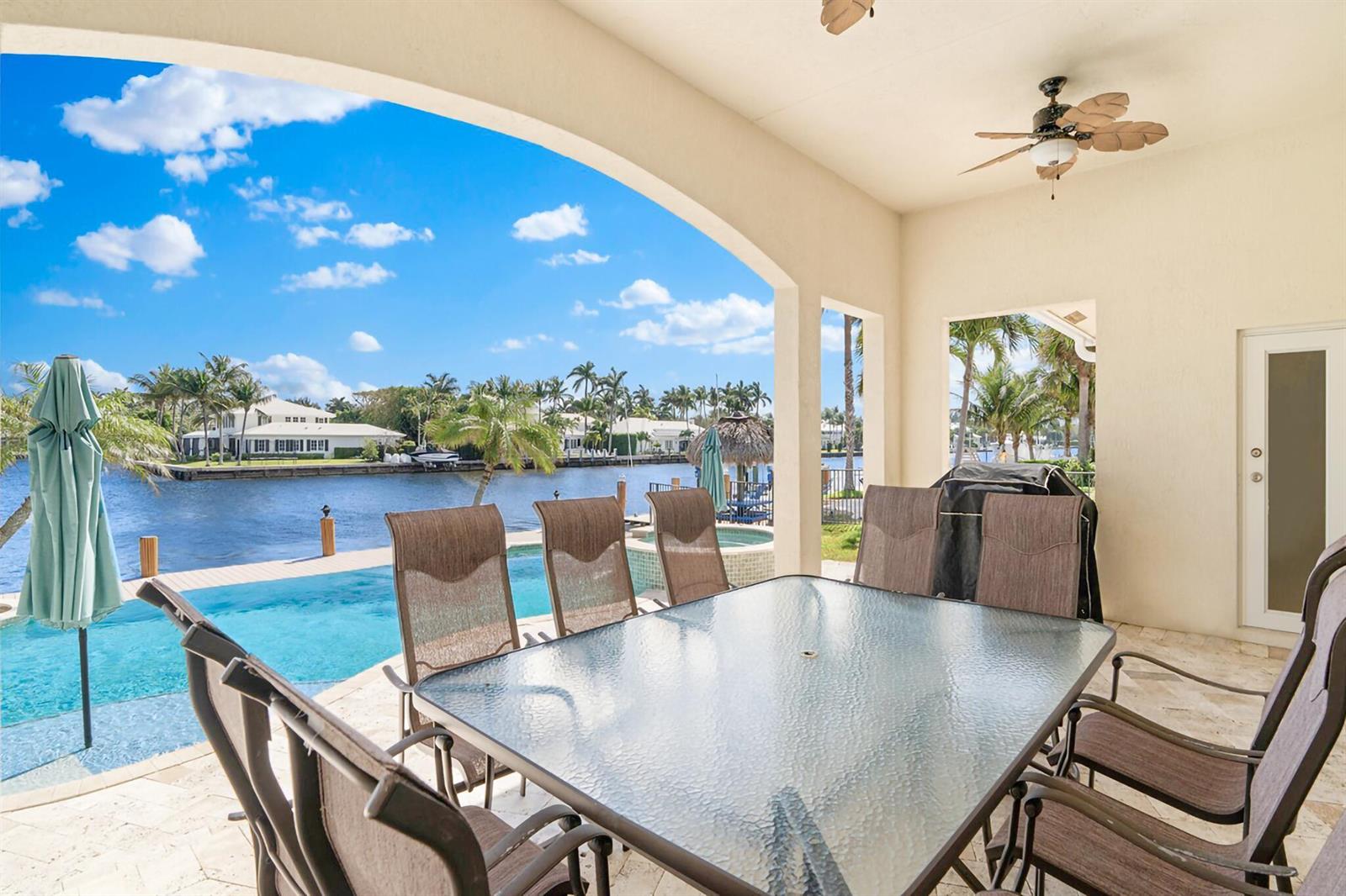 A covered patio features a glass-top dining table overlooking a swimming pool and canal — 3219 Karen Drive, Delray Beach FL 33483, DELRAY BEACH, FL