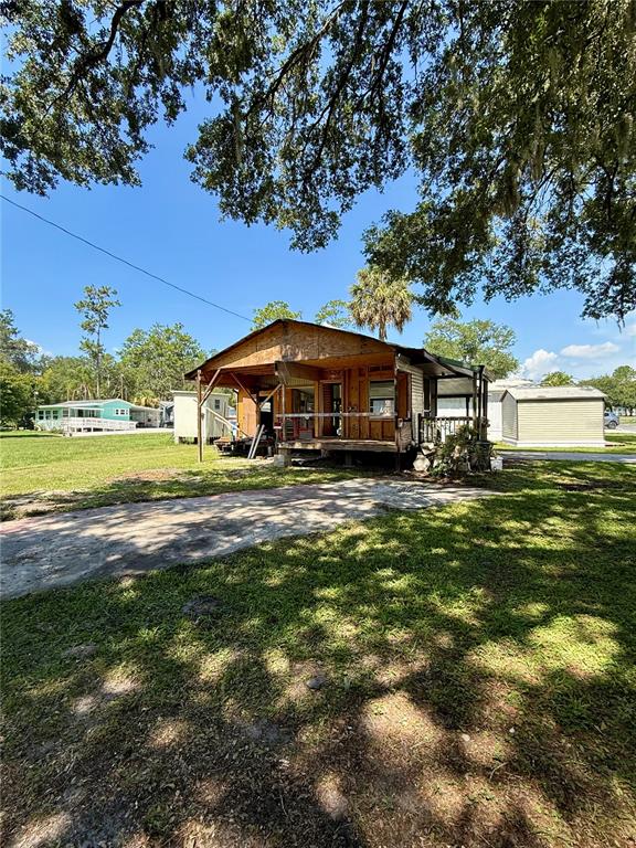 A weathered, unfinished wooden structure stands on a grassy lot under large oak trees — 2092 CULBREATH ROAD UNIT D24, BROOKSVILLE, FL