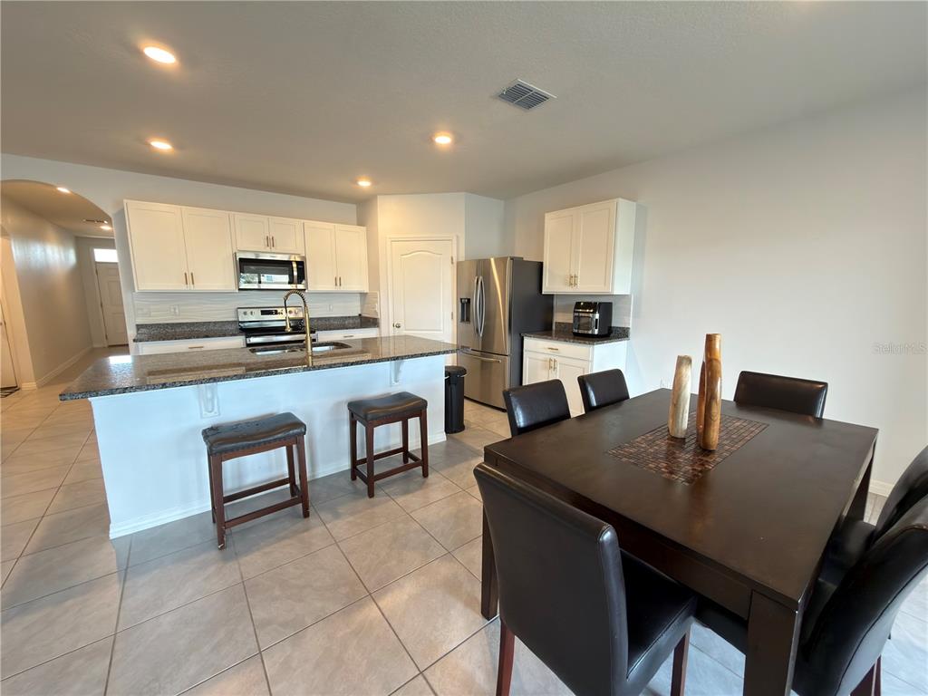 A kitchen with white cabinets, granite countertops, and a dining area with a dark table — 4079 ALISSA LANE, HAINES CITY, FL