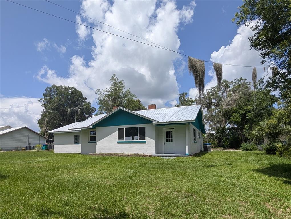A white brick house with a teal gable and a metal roof sits on grass — 414 S PROSPECT STREET, CRESCENT CITY, FL