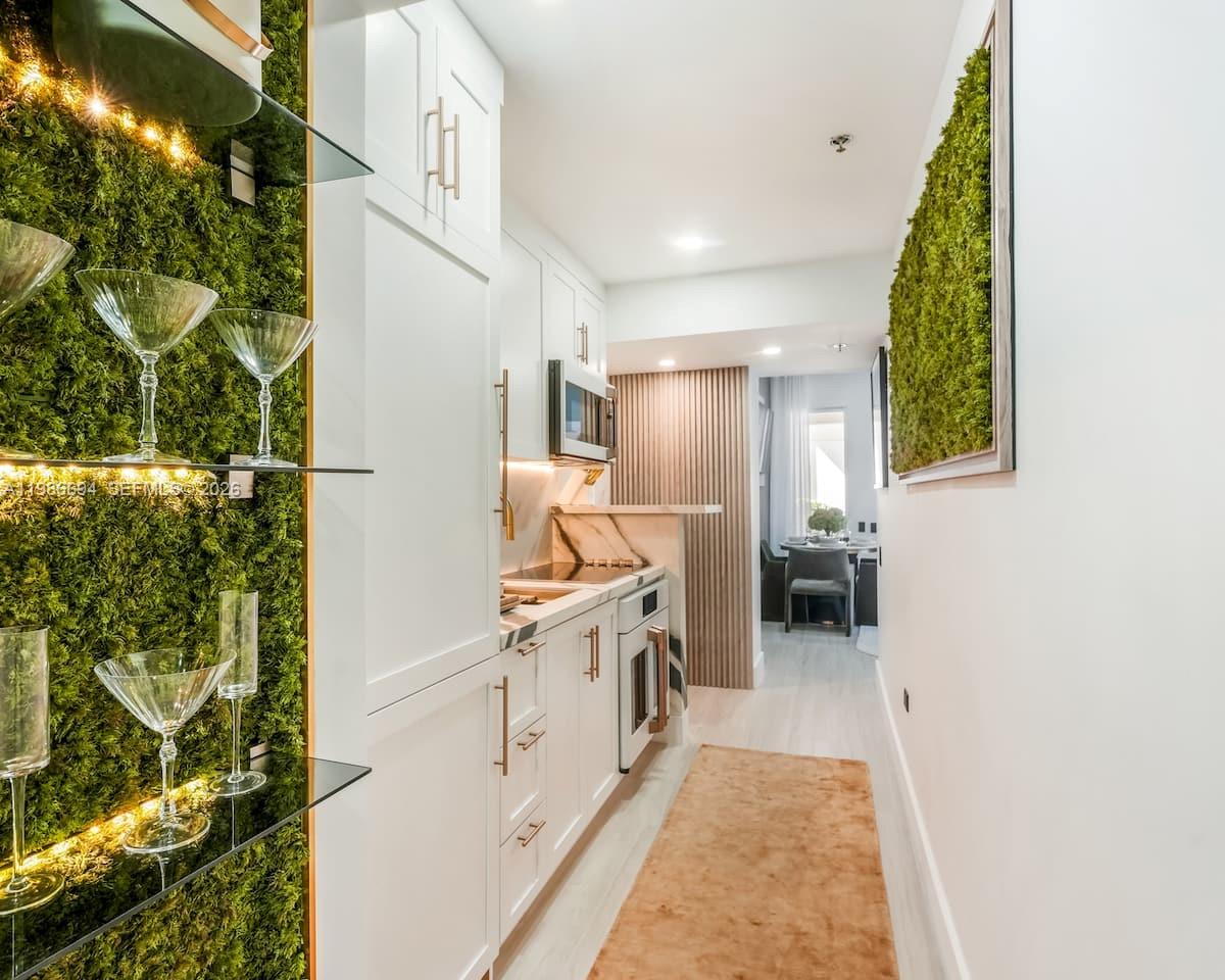 A narrow kitchen features white cabinets, marble countertops, glass shelving, and a moss wall accent — 100 Collins Ave # 202, Miami Beach FL 33139, MIAMI BEACH, FL