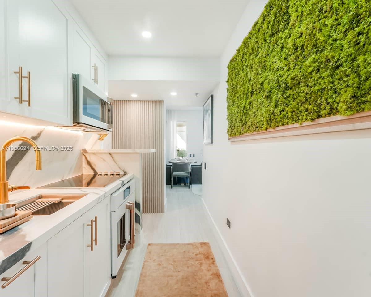 A galley kitchen features white cabinetry, marble-style countertops, and a decorative moss wall — 100 Collins Ave # 202, Miami Beach FL 33139, MIAMI BEACH, FL
