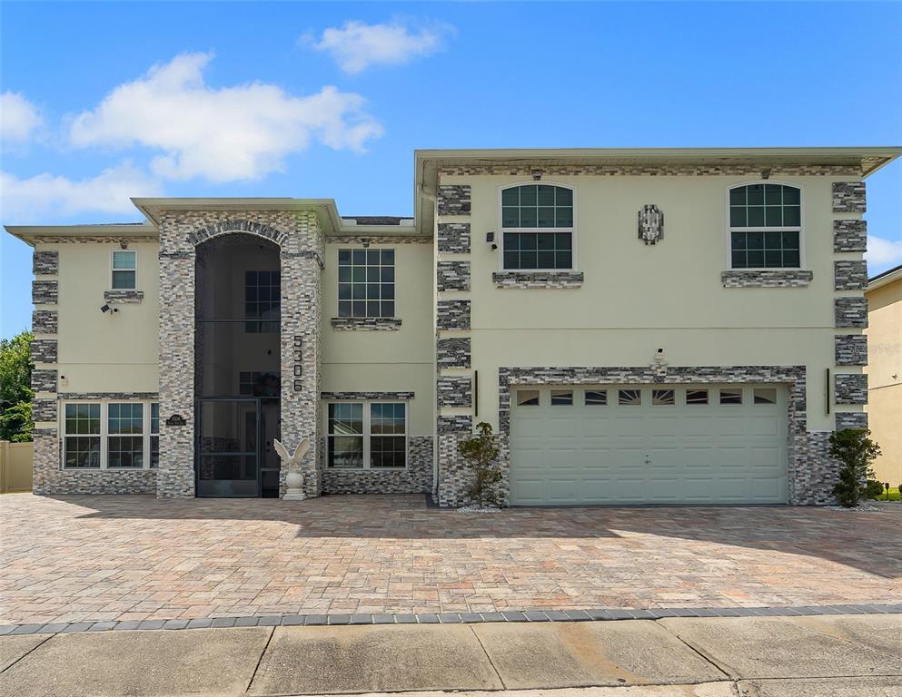 A two-story house features a stone-accented facade, a large arched entryway, and a paved driveway — 5306 CORAL VINE LANE, KISSIMMEE, FL