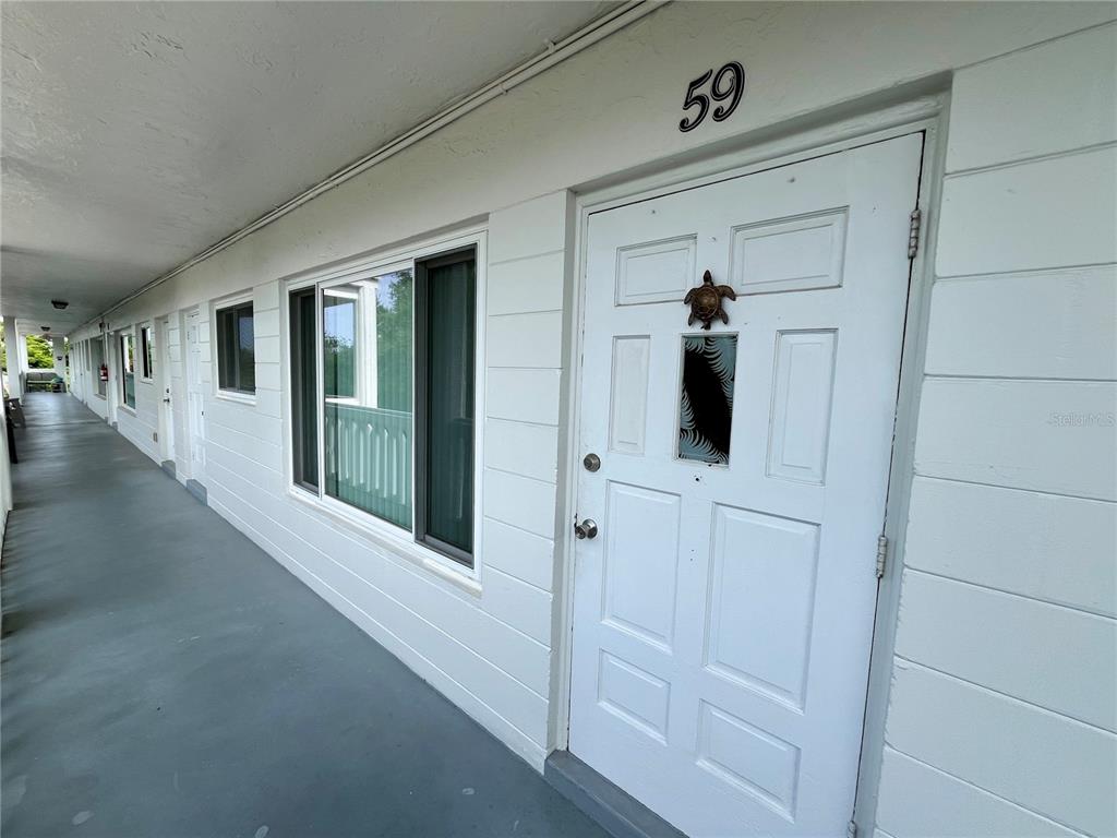 An exterior view of a white door marked 59 along an outdoor apartment walkway — 2021 AUSTRALIA WAY W UNIT 59, CLEARWATER, FL