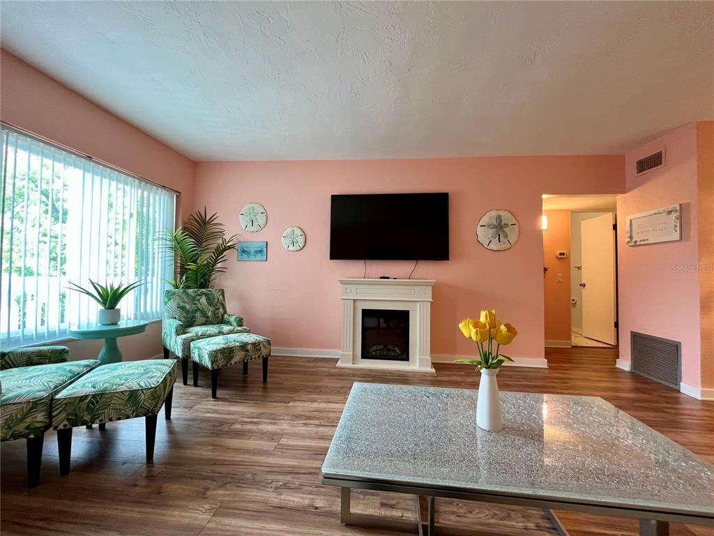 A living room features peach walls, wood-look flooring, a fireplace, and tropical-patterned armchairs — 2021 AUSTRALIA WAY W UNIT 59, CLEARWATER, FL