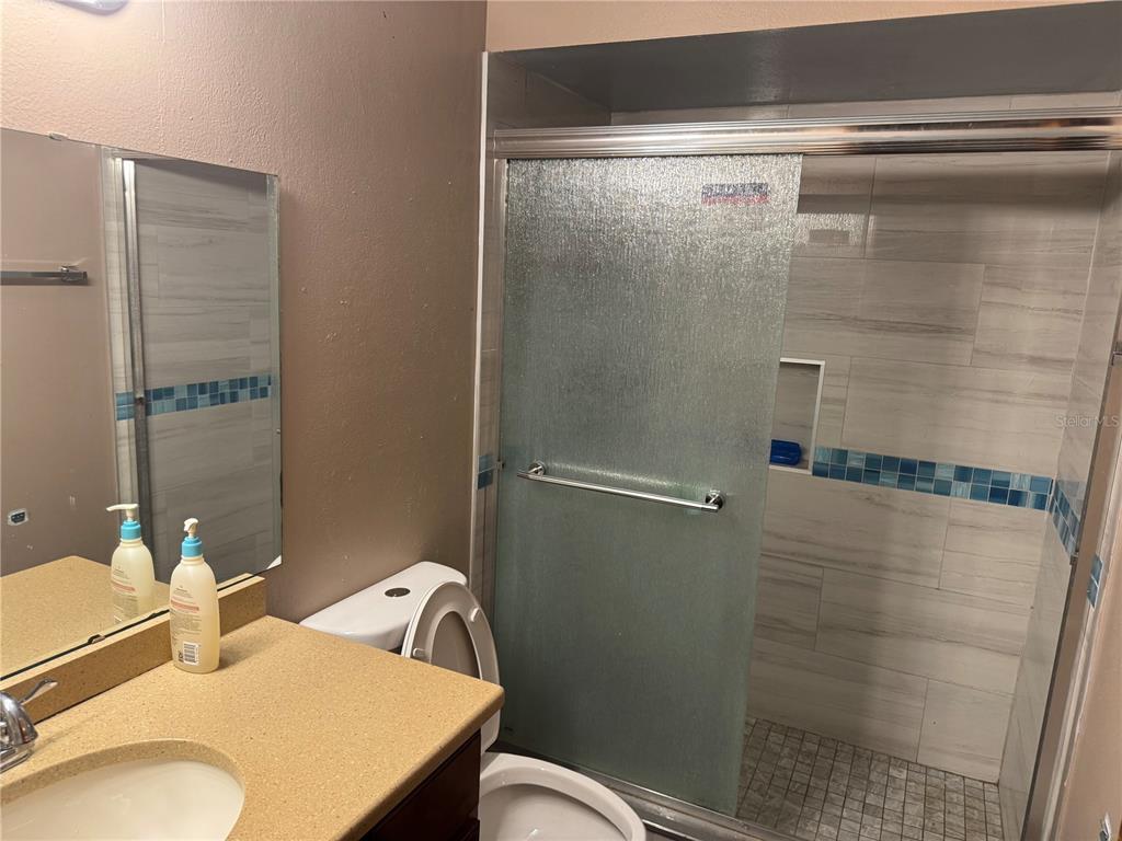 A bathroom features a tan vanity, a toilet, and a walk-in shower with tiled walls — 1410 MONITOR AVENUE, ORLANDO, FL