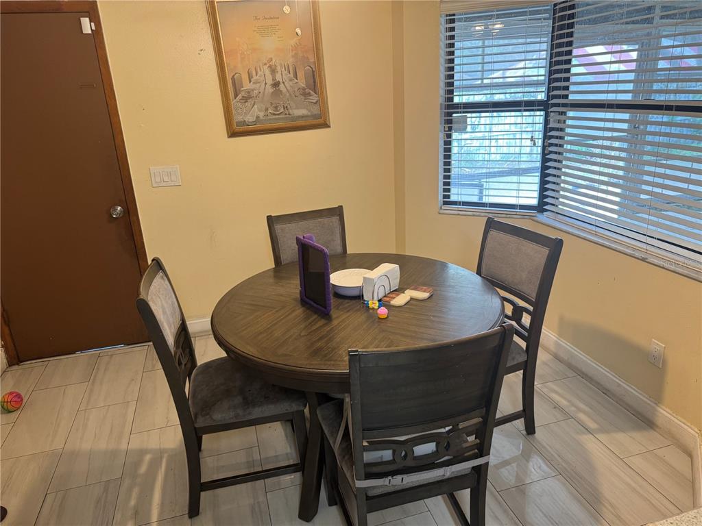 A dining area features a round wooden table with four chairs on light-colored tile flooring — 1410 MONITOR AVENUE, ORLANDO, FL