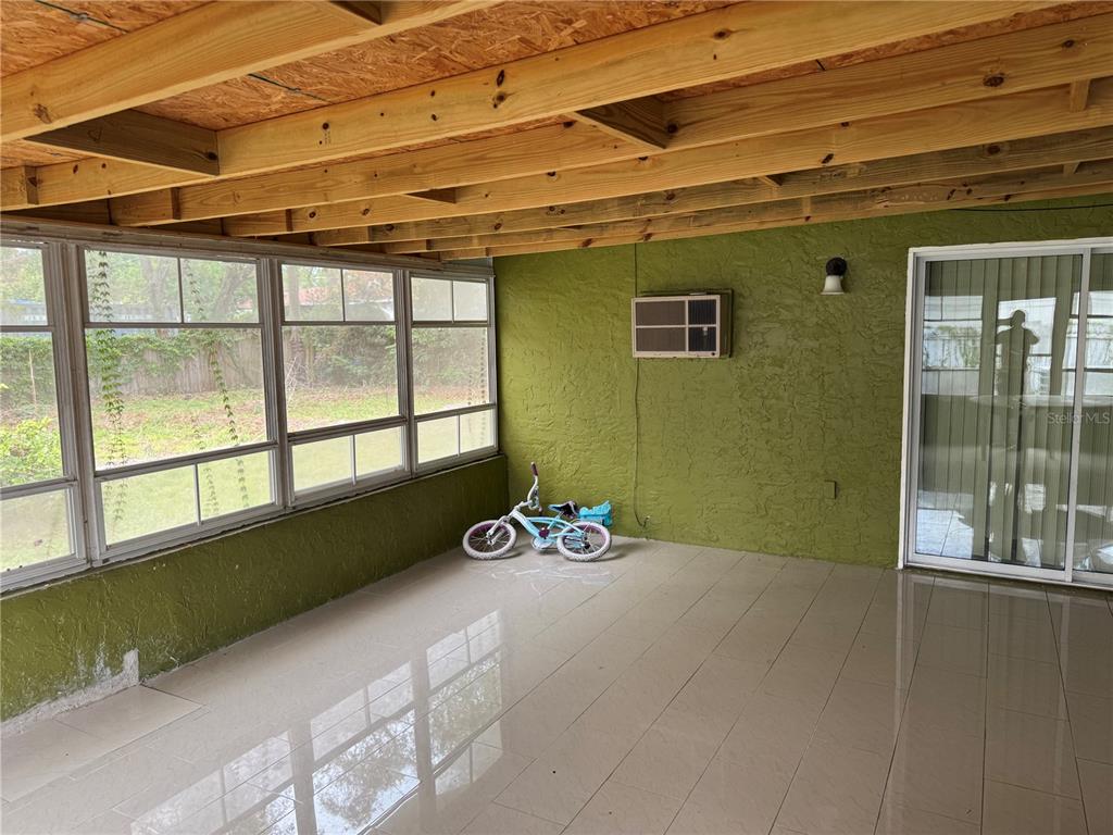 A sunroom with tiled floors, exposed wooden ceiling beams, and a small child's bicycle — 1410 MONITOR AVENUE, ORLANDO, FL