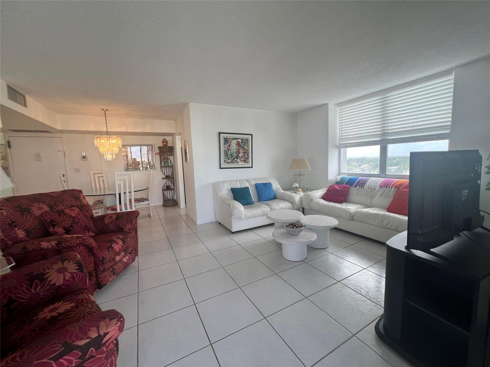 A living room with white tile floors, white sofas, and a dining area with a chandelier — 101 Briny Avenue # 811, Pompano Beach FL 33062, POMPANO BEACH, FL