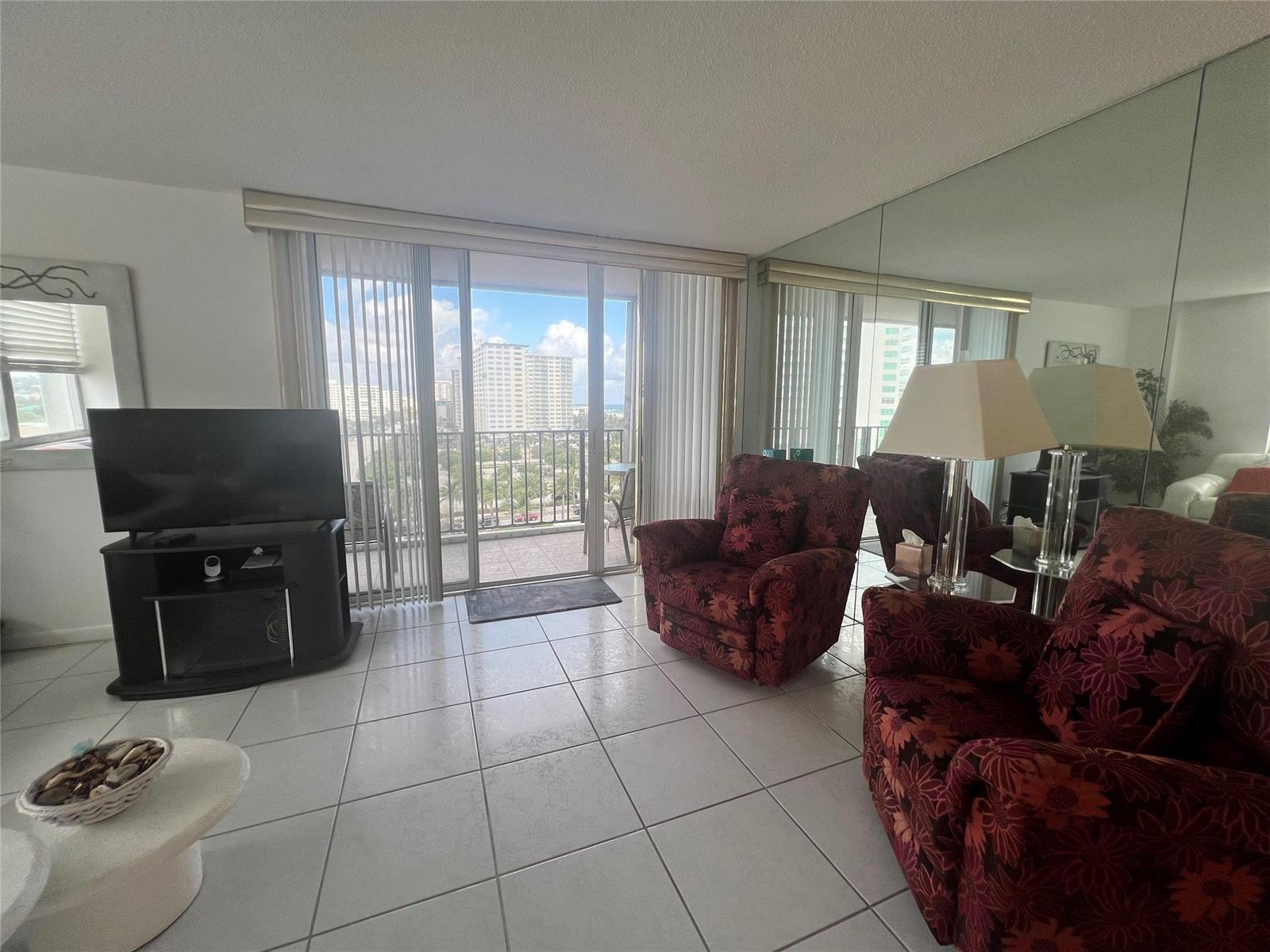 A living room with tile floors, floral armchairs, a television, and a balcony view — 101 Briny Avenue # 811, Pompano Beach FL 33062, POMPANO BEACH, FL