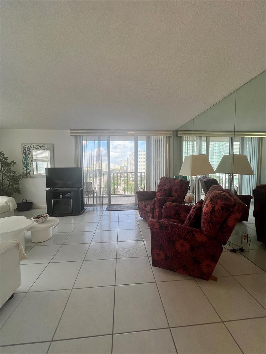 A living room with white tile floors, floral armchairs, and a balcony overlooking city buildings — 101 Briny Avenue # 811, Pompano Beach FL 33062, POMPANO BEACH, FL
