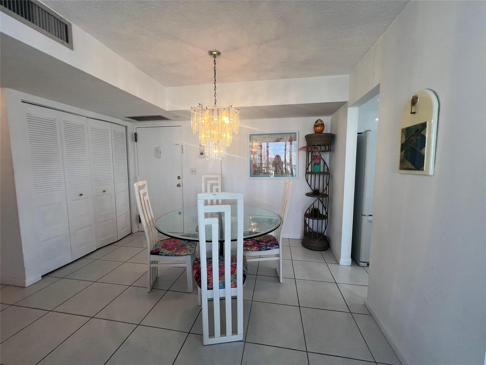 A dining area features a glass-topped table, white chairs, and a crystal chandelier — 101 Briny Avenue # 811, Pompano Beach FL 33062, POMPANO BEACH, FL