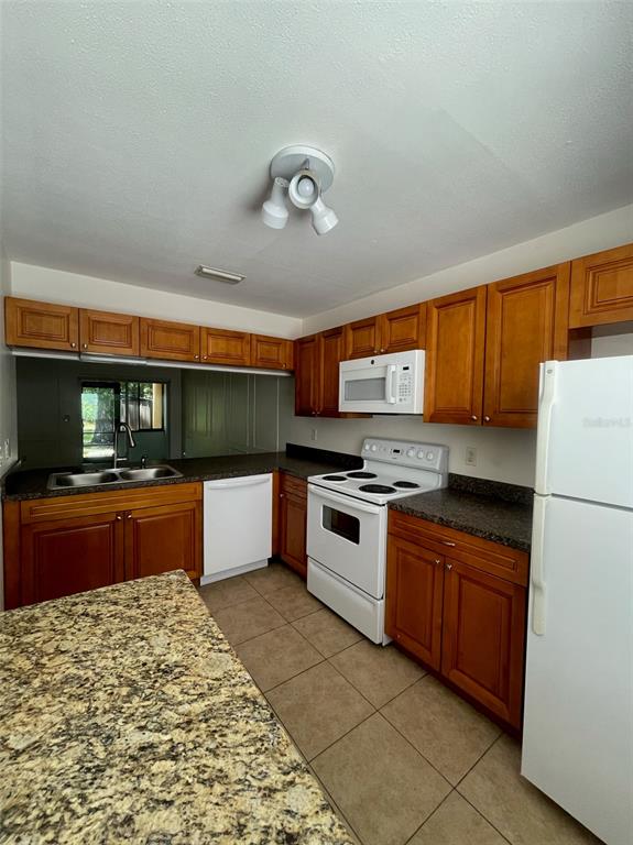 A kitchen features wood cabinets, granite countertops, white appliances, and tile flooring — 950 BELTREES STREET, DUNEDIN, FL