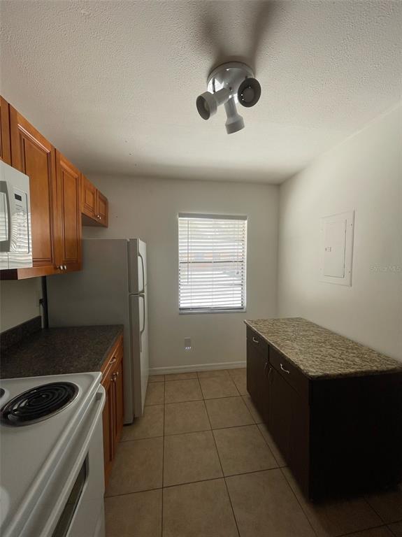 A kitchen features wood cabinets, a white refrigerator, a granite-topped island, and tile flooring — 950 BELTREES STREET, DUNEDIN, FL