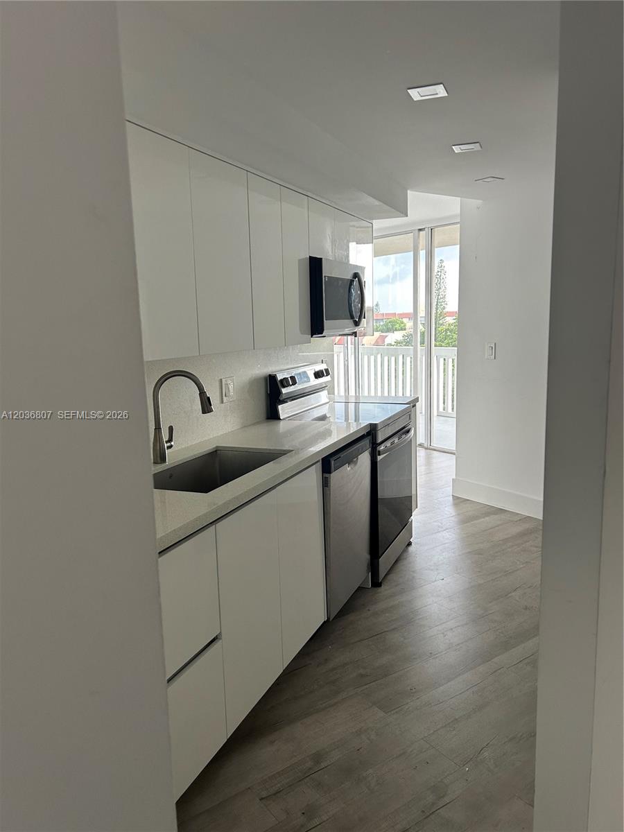 A galley-style kitchen features white cabinets, stainless steel appliances, and light-colored countertops — 6921 Environ Blvd # 7P, Lauderhill FL 33319, LAUDERHILL, FL