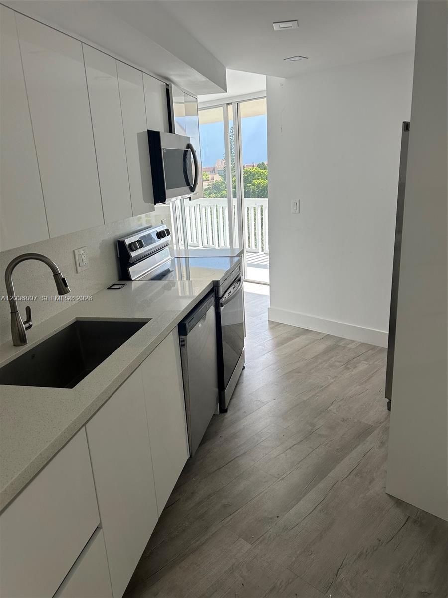 A modern kitchen features white cabinets, stainless steel appliances, and light wood-look flooring — 6921 Environ Blvd # 7P, Lauderhill FL 33319, LAUDERHILL, FL