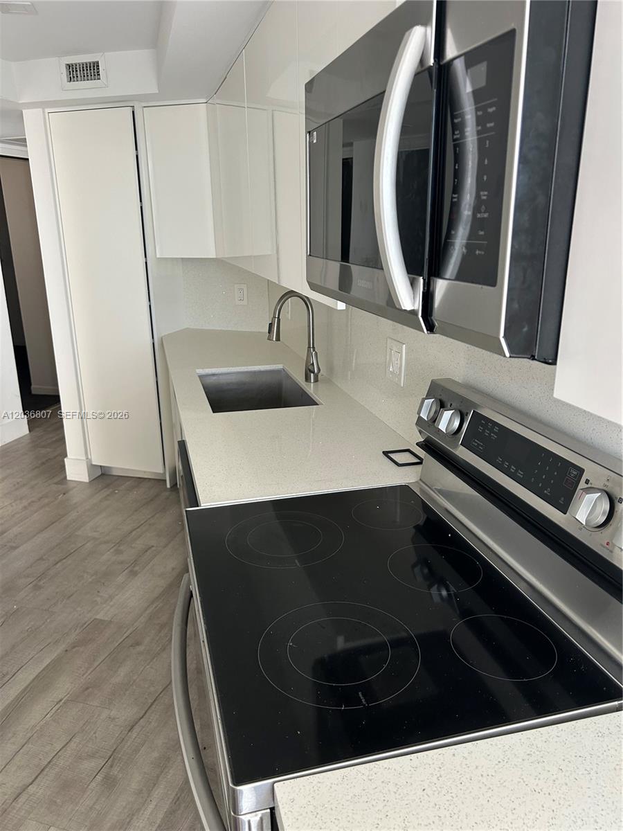 A modern kitchen features white cabinets, stainless steel appliances, and light-colored quartz countertops — 6921 Environ Blvd # 7P, Lauderhill FL 33319, LAUDERHILL, FL