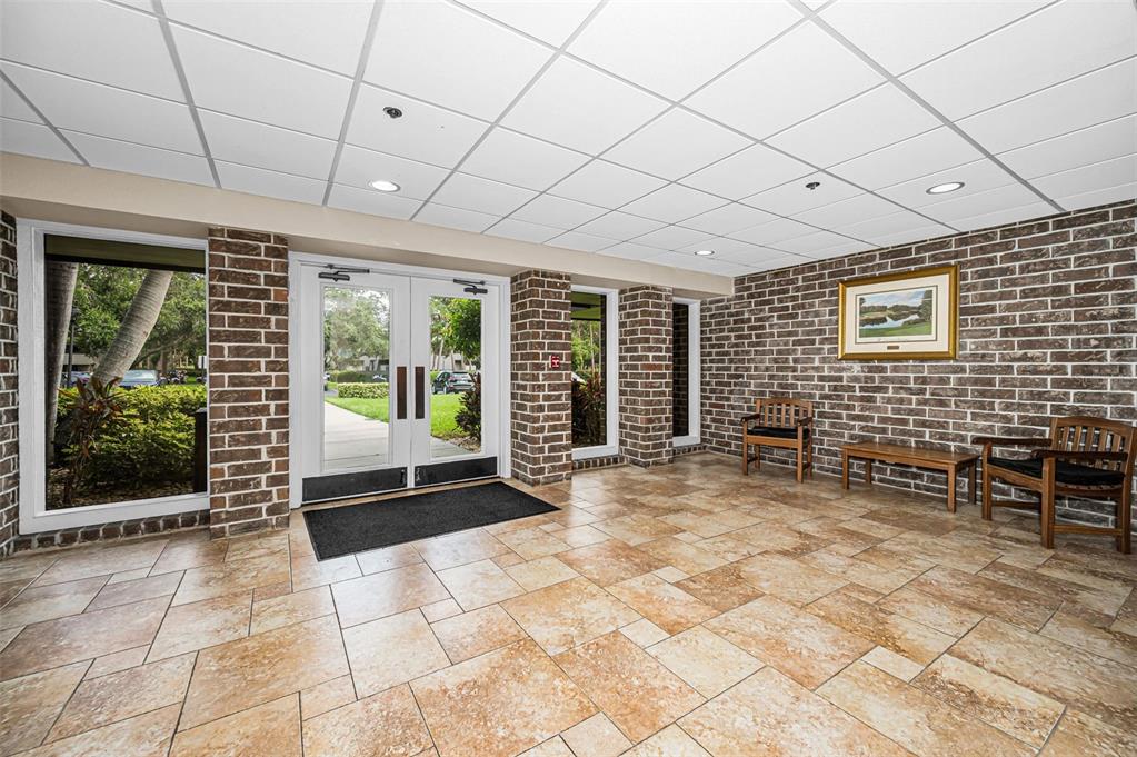 A lobby with tile flooring, brick walls, a drop ceiling, and double glass entry doors — 36750 US HIGHWAY 19 N UNIT 20-117, PALM HARBOR, FL