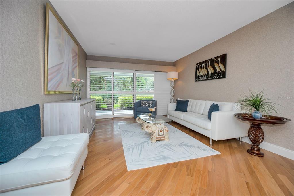 A living room features hardwood floors, a white sofa, an elephant-base coffee table, and sliding doors — 36750 US HIGHWAY 19 N UNIT 20-117, PALM HARBOR, FL