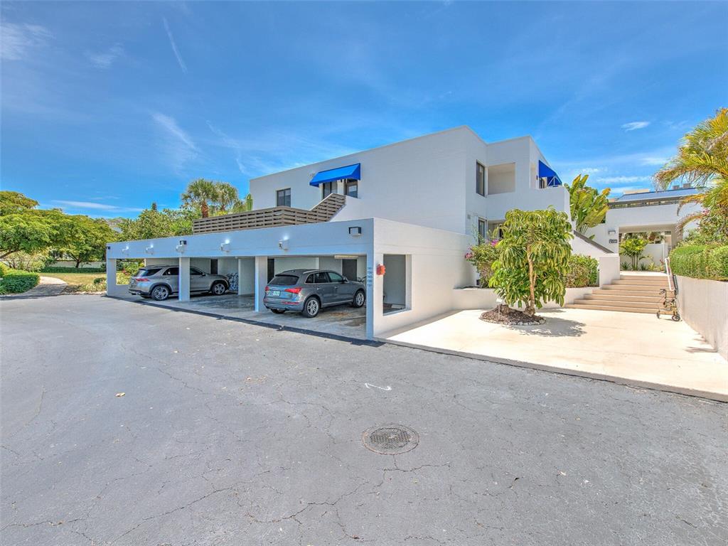 A white multi-story building features a covered parking area with two parked cars — 739 BAYPORT WAY UNIT 739, LONGBOAT KEY, FL