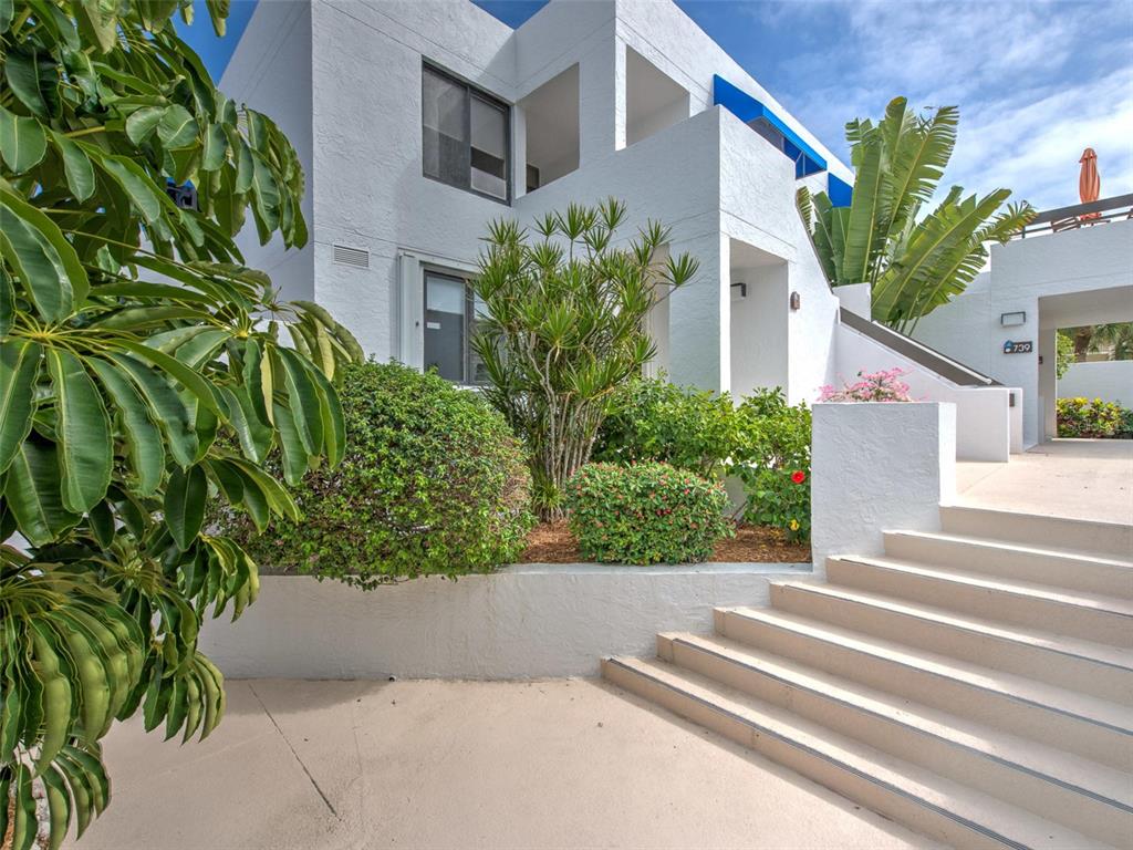 A white multi-story building exterior features concrete stairs leading to an entrance with lush landscaping — 739 BAYPORT WAY UNIT 739, LONGBOAT KEY, FL