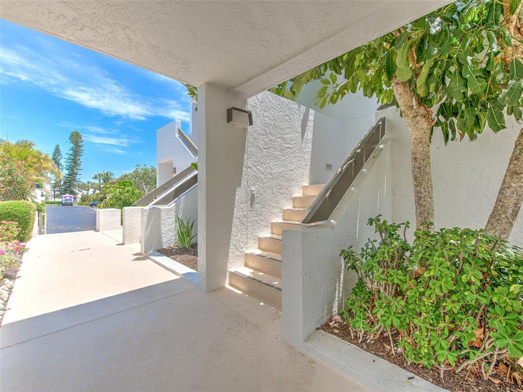 An outdoor covered walkway leads to a set of concrete stairs beside a landscaped tree — 739 BAYPORT WAY UNIT 739, LONGBOAT KEY, FL