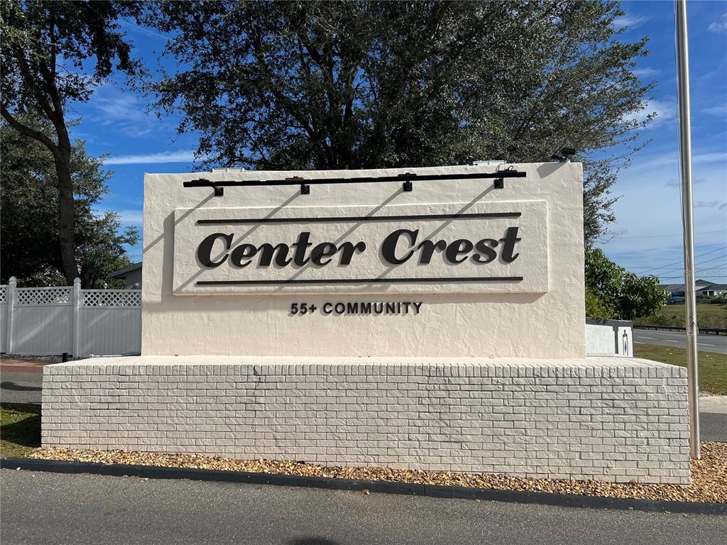 A beige masonry sign for Center Crest 55+ Community stands outdoors under a blue sky — 443 PANSY STREET, DAVENPORT, FL