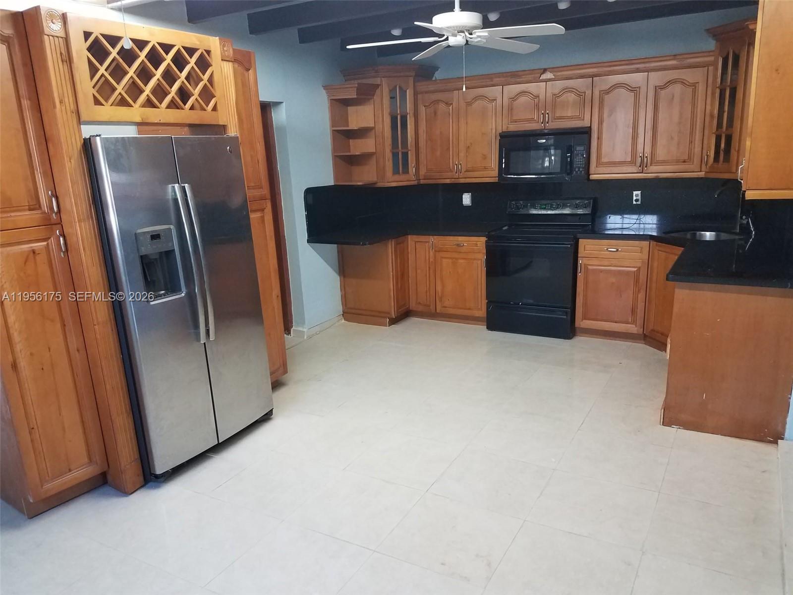 A kitchen features wooden cabinets, black countertops, a stainless steel refrigerator, and a ceiling fan — 2828 SW 3rd St, Miami FL 33135, MIAMI, FL