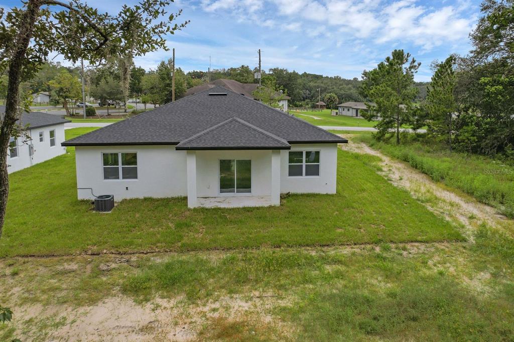 The back exterior of a white, single-story house with a dark shingled roof and lawn — 205 AUSTRALIAN DRIVE, ROTONDA WEST, FL