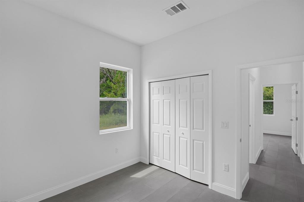 A bedroom with white walls, gray tile flooring, a window, and a white closet — 205 AUSTRALIAN DRIVE, ROTONDA WEST, FL