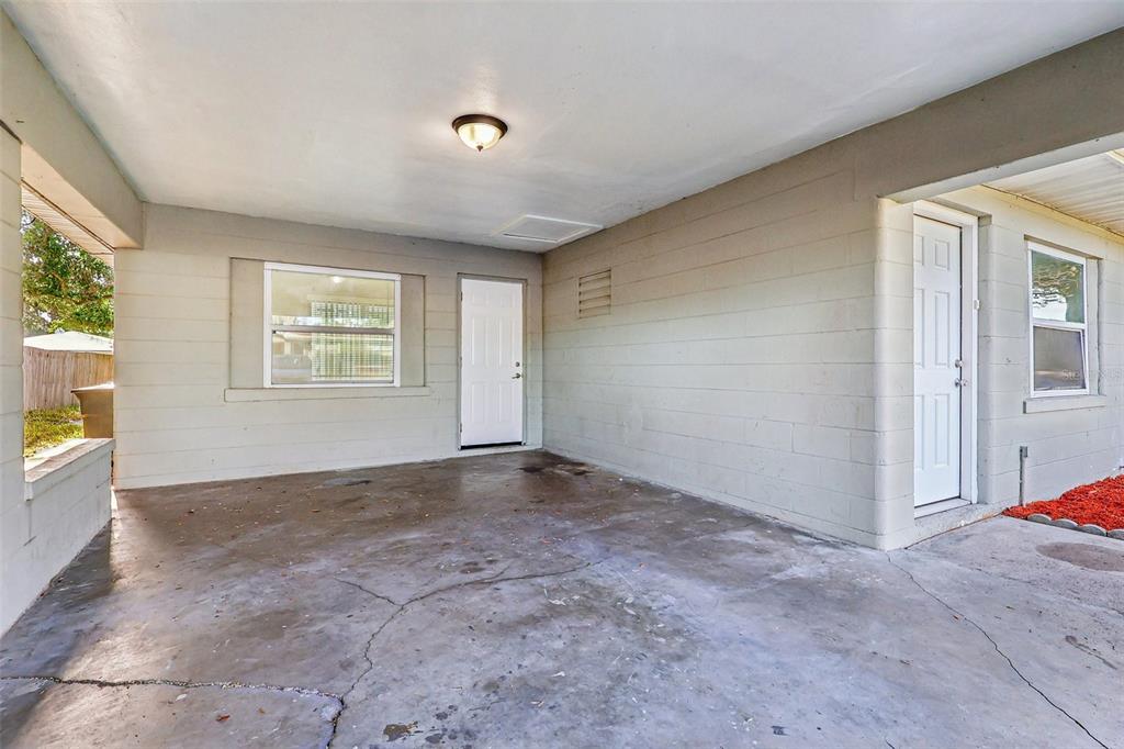 A concrete carport features two white doors, a window, and a ceiling light fixture — 1680 32ND STREET NW, WINTER HAVEN, FL