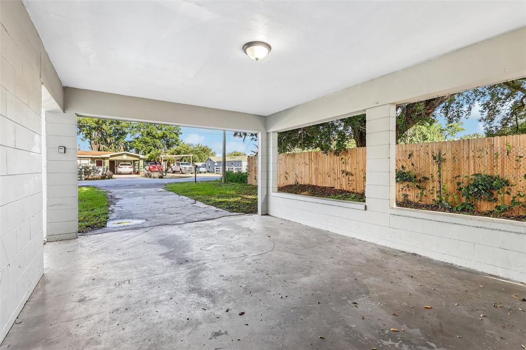 An open-air carport with a concrete floor, white block walls, and a wooden fence exterior — 1680 32ND STREET NW, WINTER HAVEN, FL