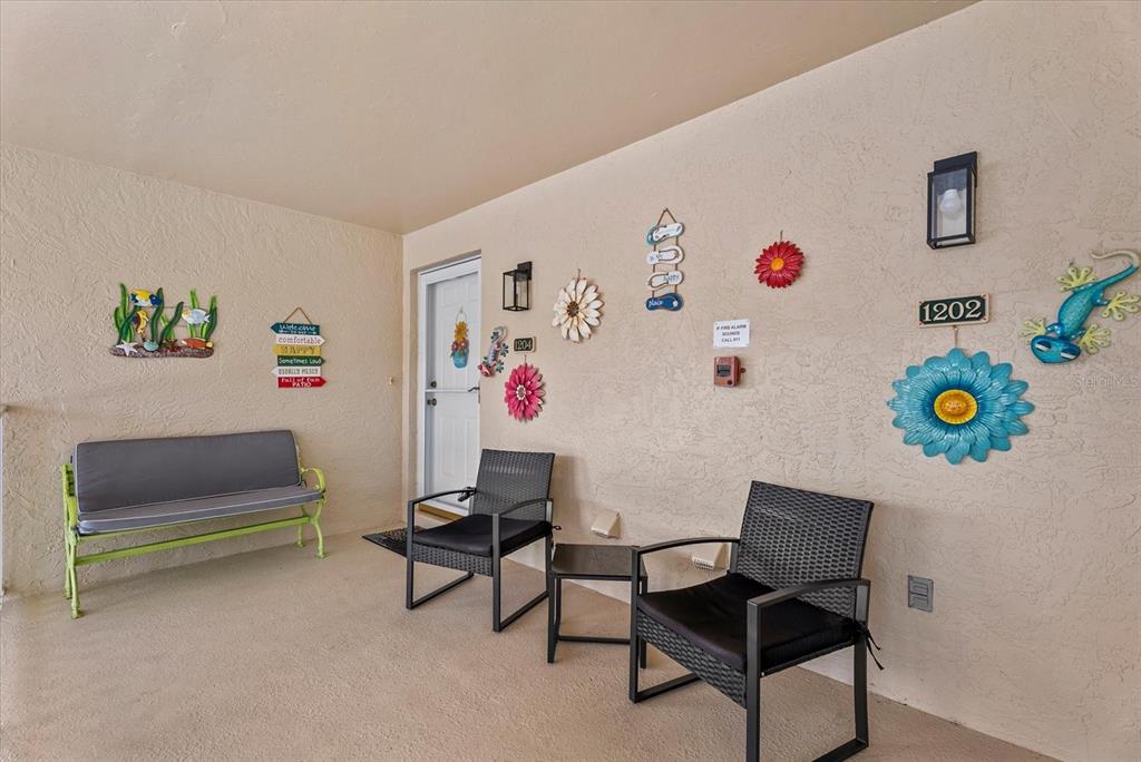 A covered patio features a bench, two chairs, a small table, and colorful wall decorations — 5800 SABAL TRACE DRIVE UNIT 1204, NORTH PORT, FL