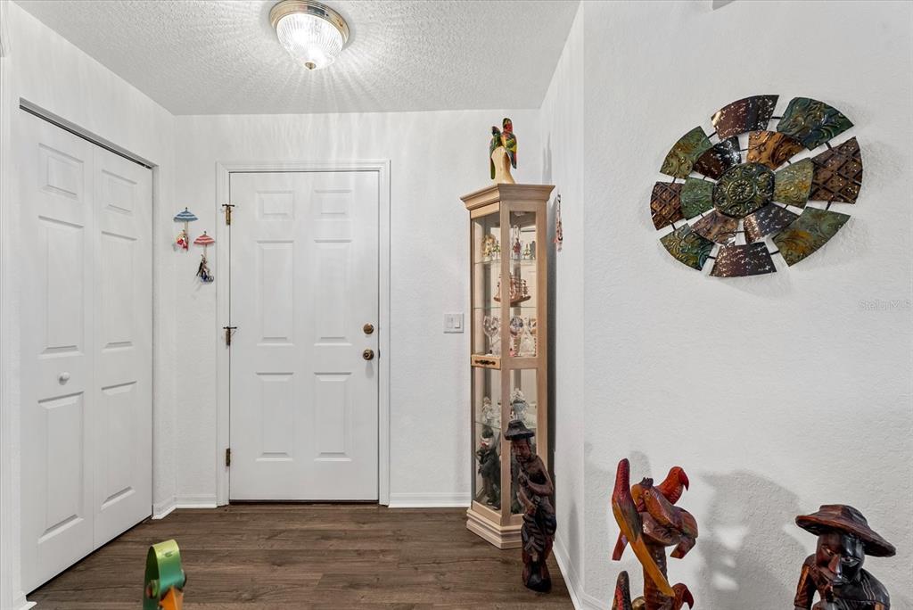 An entryway features wood-look flooring, a white door, a glass display cabinet, and wall decor — 5800 SABAL TRACE DRIVE UNIT 1204, NORTH PORT, FL