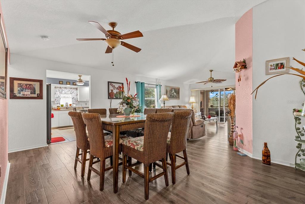 A dining area with wicker chairs sits in an open-concept room with wood-look flooring — 5800 SABAL TRACE DRIVE UNIT 1204, NORTH PORT, FL