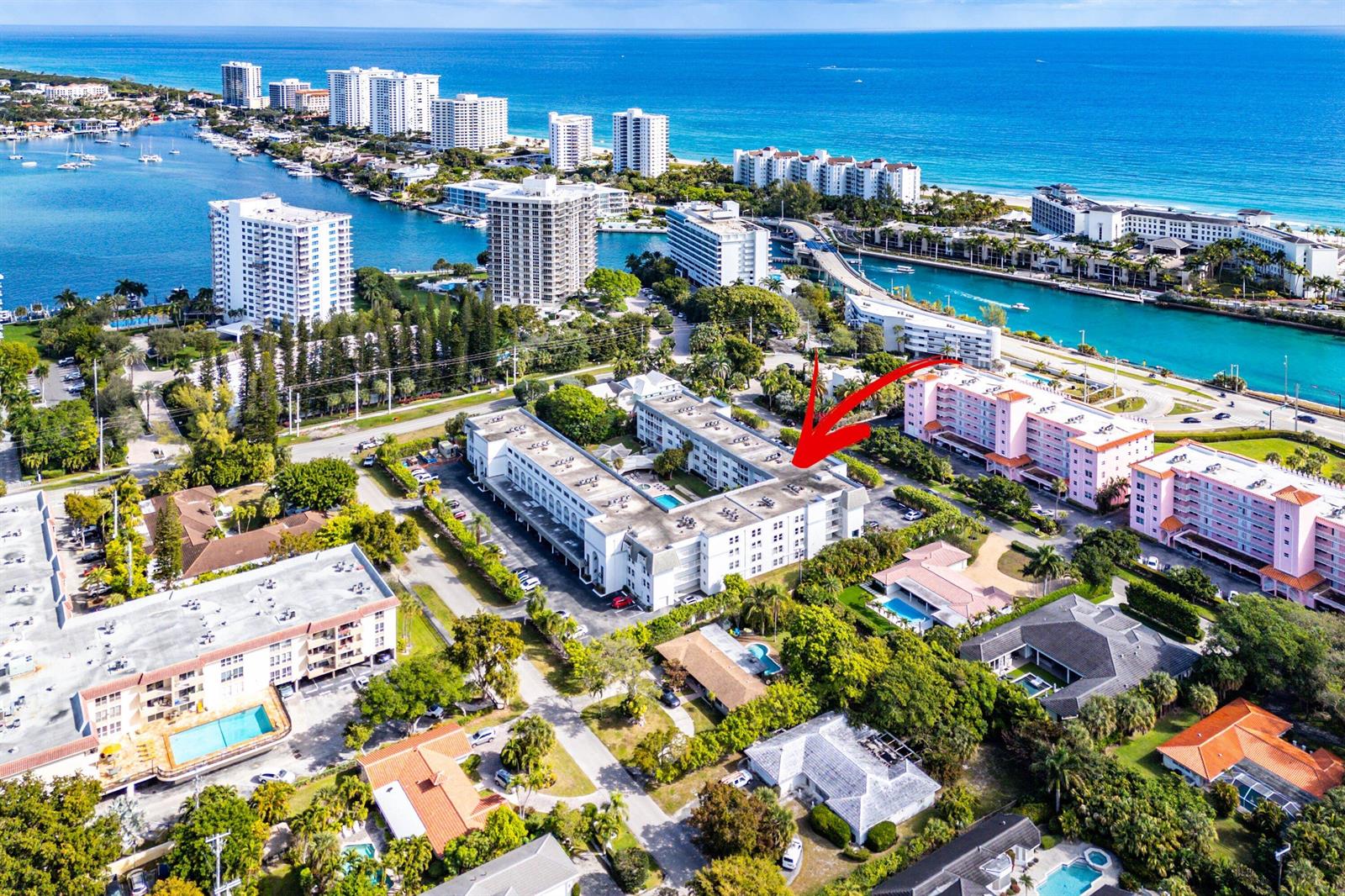 An aerial view shows a multi-story white apartment complex surrounded by trees and nearby buildings — 800 E Camino Real # 409, Boca Raton FL 33432, BOCA RATON, FL