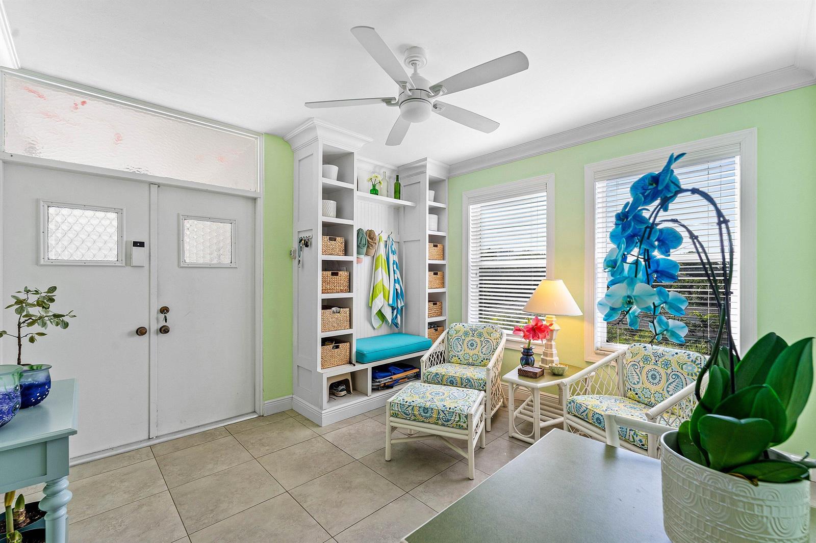 A sunroom features light green walls, tile flooring, a built-in storage unit, and wicker furniture — 800 E Camino Real # 409, Boca Raton FL 33432, BOCA RATON, FL