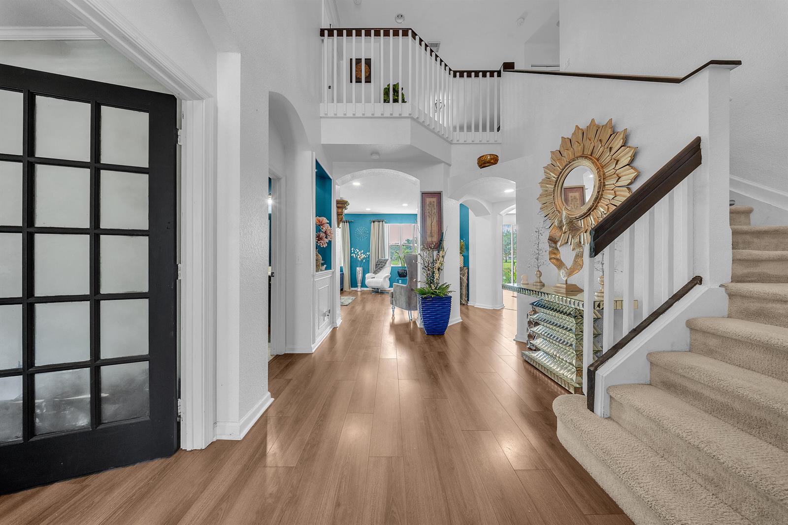 A bright foyer features wood flooring, a carpeted staircase, and a view into a blue room — 726 Gazetta Way, West Palm Beach FL 33413, WEST PALM BEACH, FL
