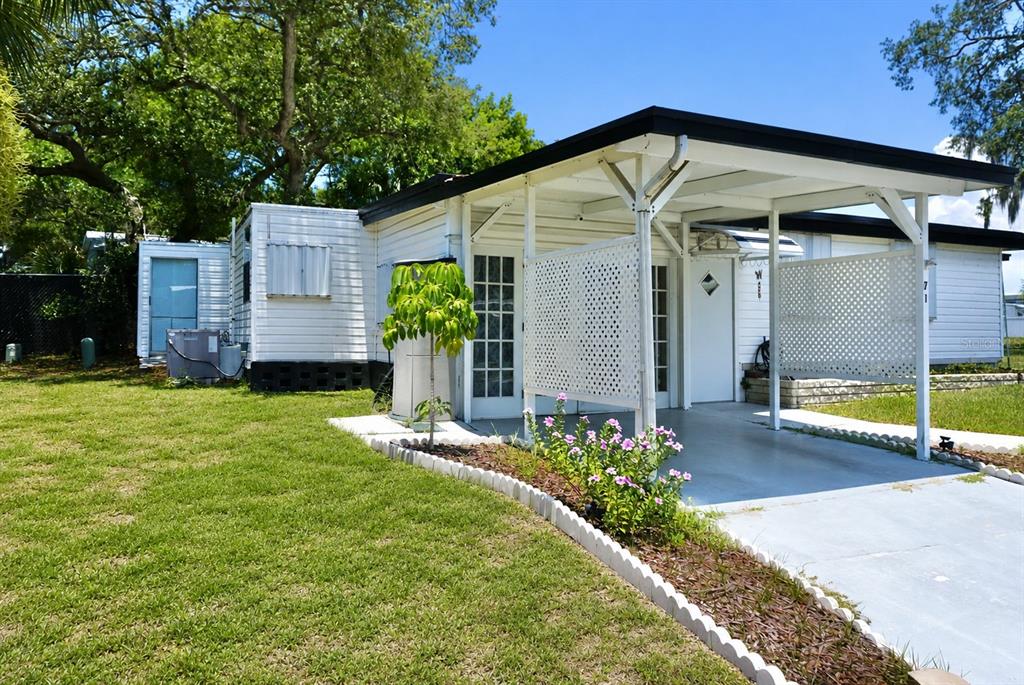 A white mobile home with a carport, lattice privacy screen, and a landscaped front yard — 980 7TH STREET NW UNIT 71, LARGO, FL