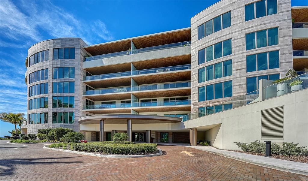 A modern multi-story apartment building features a circular driveway entrance and expansive glass balconies — 1561 GULF OF MEXICO DRIVE UNIT 304, LONGBOAT KEY, FL
