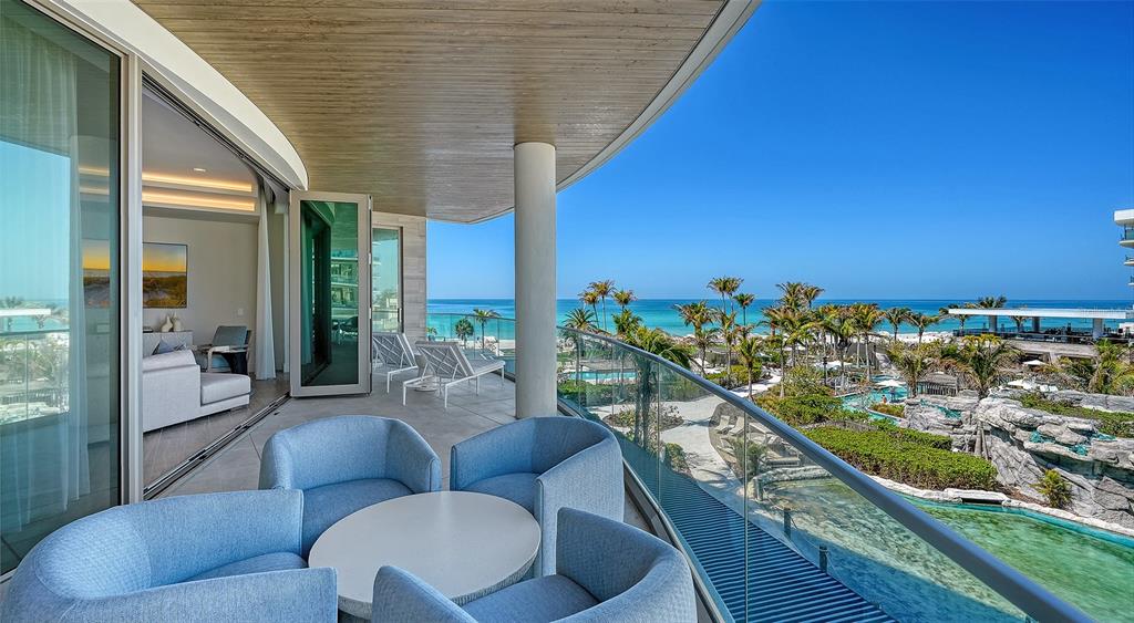 A balcony with blue chairs and a table overlooks a resort pool and the ocean — 1561 GULF OF MEXICO DRIVE UNIT 304, LONGBOAT KEY, FL