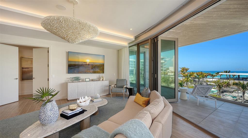 A living room features a textured chandelier, a curved sofa, and folding doors opening to a balcony — 1561 GULF OF MEXICO DRIVE UNIT 304, LONGBOAT KEY, FL