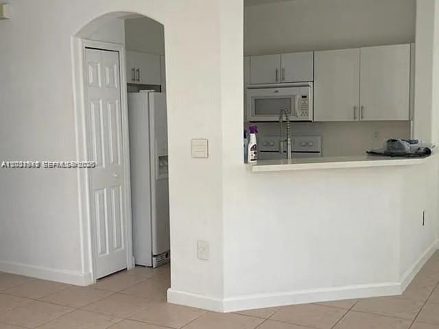 A kitchen with white cabinets and appliances features a breakfast bar opening to a room — 7778 NW 116th Ave # 0, Doral FL 33178, DORAL, FL