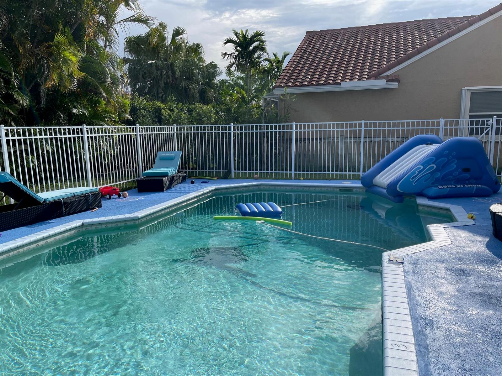 A backyard swimming pool with a blue slide, lounge chairs, and a white metal fence — 9460 Lake Serena Drive, Boca Raton FL 33496, BOCA RATON, FL
