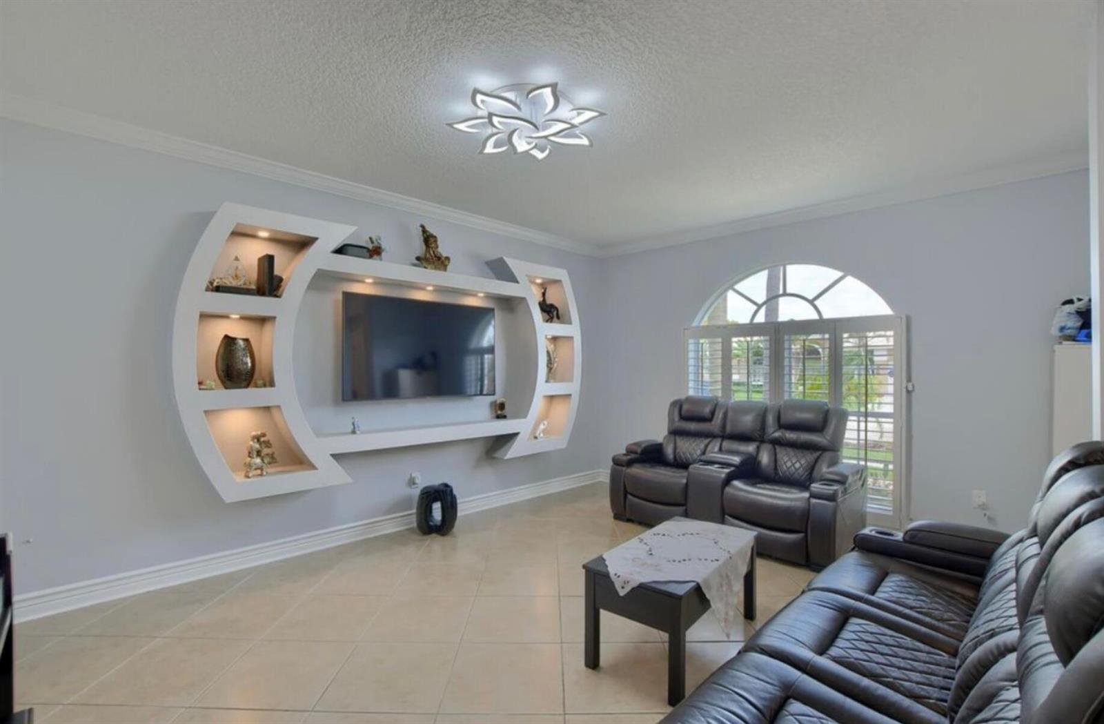 A living room features a modern white circular wall unit, leather sofas, and tile flooring — 9460 Lake Serena Drive, Boca Raton FL 33496, BOCA RATON, FL