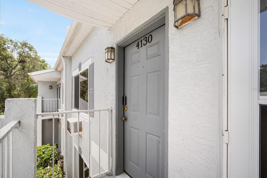 A gray front door with the number 4130 is located on an outdoor apartment balcony — 4130 DOLPHIN DRIVE UNIT 203, TAMPA, FL